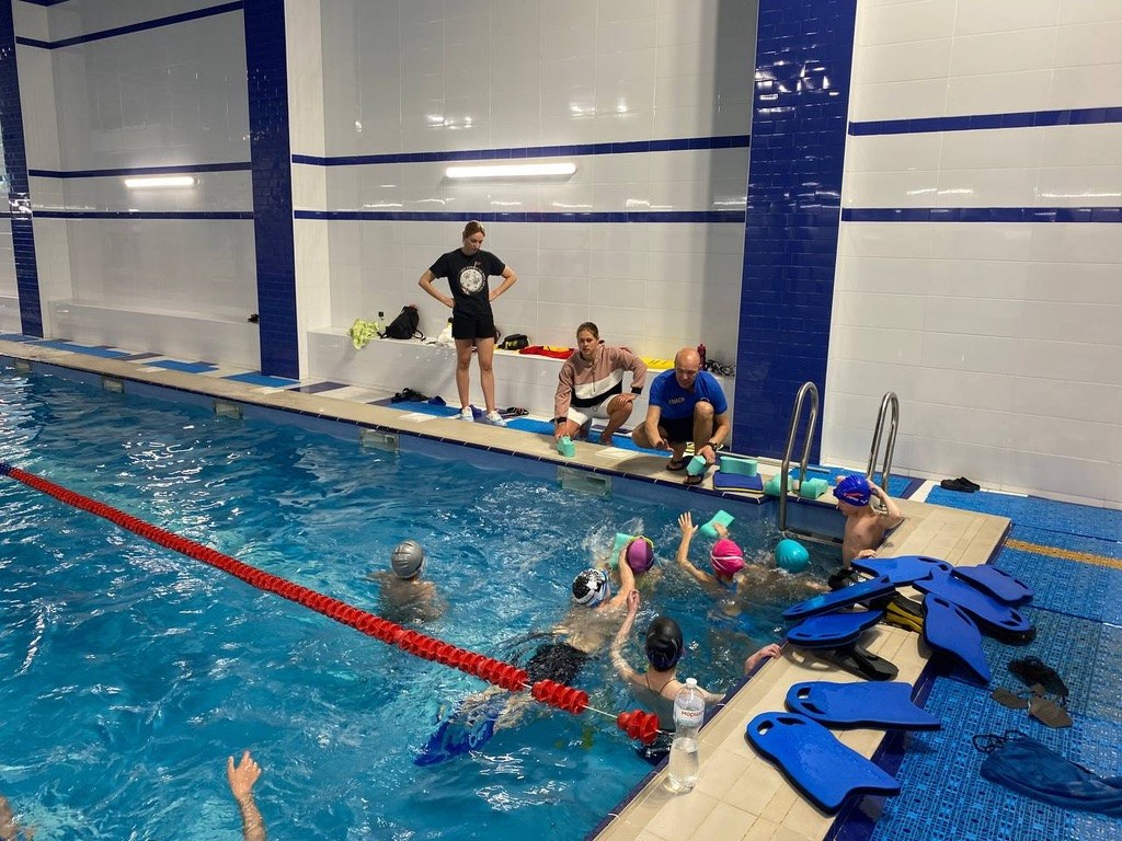 Coaches on the pool deck giving instructions to a group of young swimmers at the wall