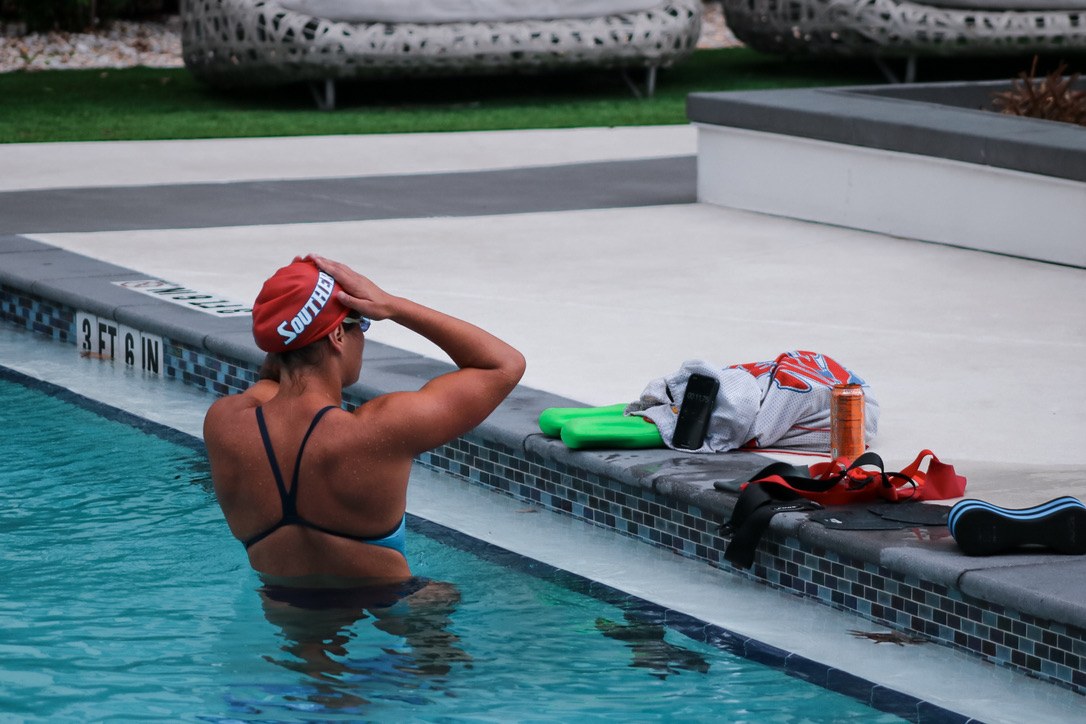 Maria at the pool wall with a kickboard, pull buoy and fins on the deck